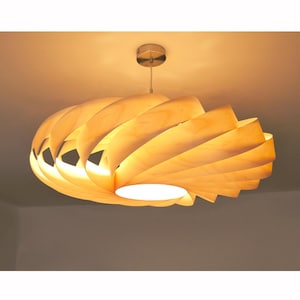 Op de afbeelding: Een moderne houten hanglamp met een spiraalvormig ontwerp. Het licht is gemaakt van gelaagde, gebogen houten panelen, waardoor een warme, omgevingsgloed ontstaat. De armatuur is opgehangen aan een zilverkleurige plafondbevestiging.