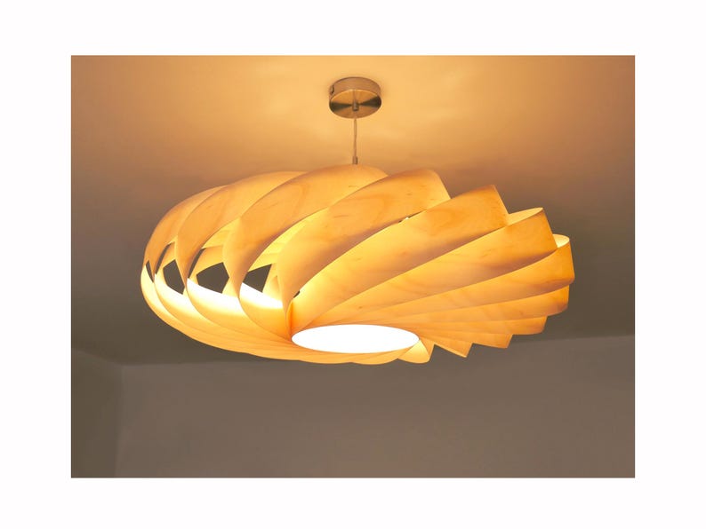 Op de afbeelding: Een moderne houten hanglamp met een spiraalvormig ontwerp. Het licht is gemaakt van gelaagde, gebogen houten panelen, waardoor een warme, omgevingsgloed ontstaat. De armatuur is opgehangen aan een zilverkleurige plafondbevestiging.