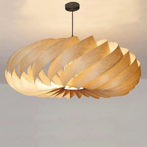Könnte beinhalten: Eine moderne Pendelleuchte aus Holz. Die Leuchte hat ein spiralförmiges Design aus geschichtetem, hellfarbigem Holz. Sie hängt an einem schwarzen Kabel und einer kreisförmigen Deckenhalterung. Das Licht ist eingeschaltet und beleuchtet die Holzschichten.