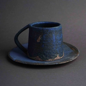 May include: A dark blue ceramic mug with a textured surface and a matching saucer. The mug has a handle and a slightly flared rim.