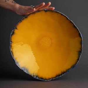 Peut inclure: Un grand bol en céramique jaune avec un bord bleu et noir. Le bol a une finition brillante et un bord légèrement irrégulier.