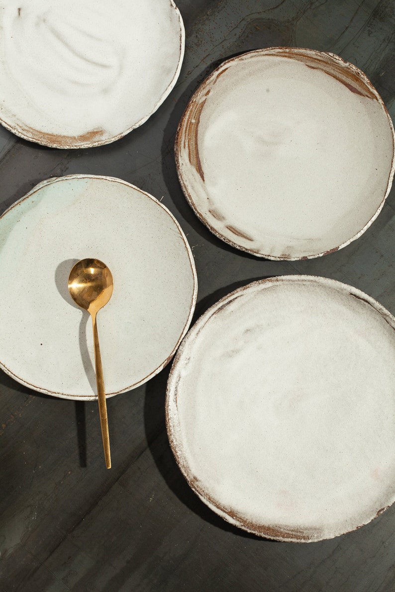 Puede incluir: Cuatro platos de cer&aacute;mica blanca con un acabado r&uacute;stico y texturado. Un plato tiene una cuchara de oro en la parte superior.