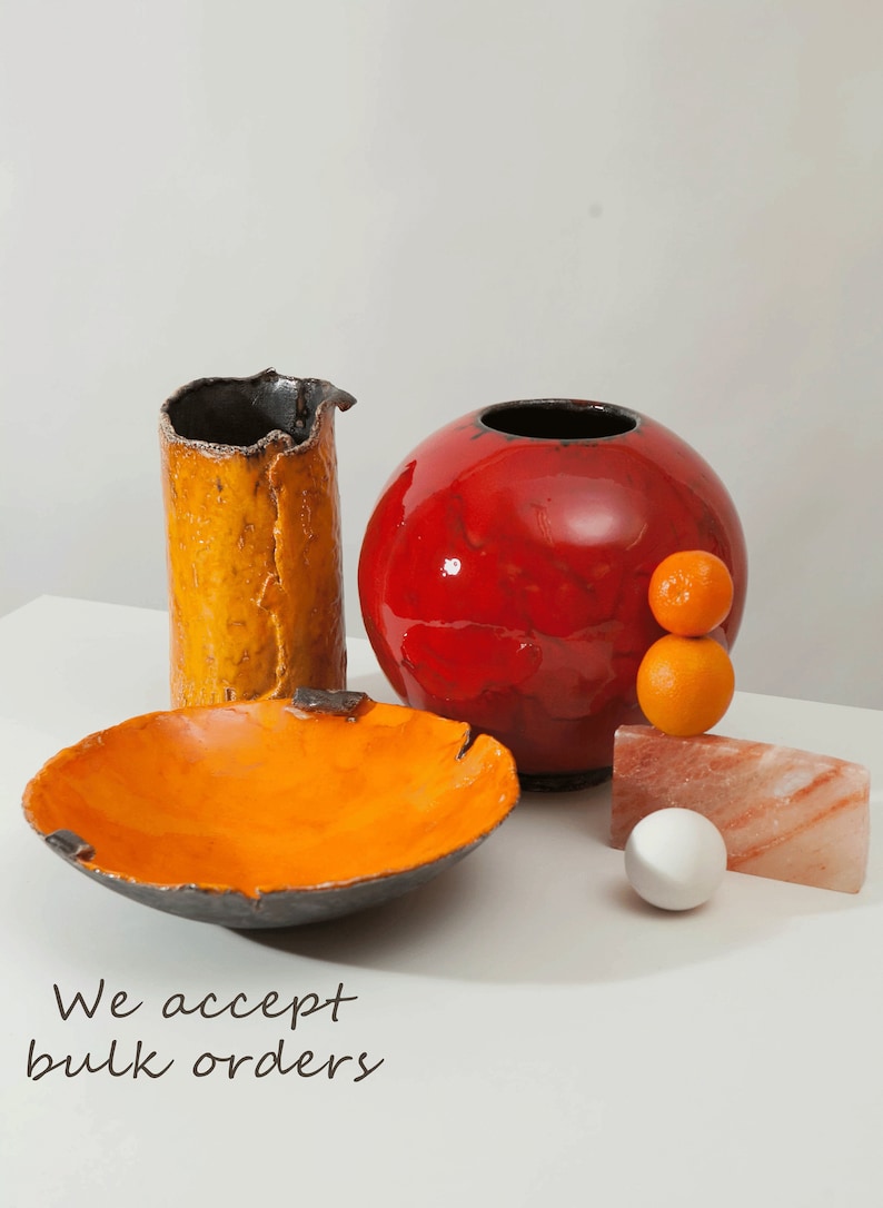 Puede incluir: Un conjunto de tres jarrones de cer&aacute;mica en naranja, rojo y negro. Los jarrones est&aacute;n todos esmaltados y tienen un aspecto r&uacute;stico y hecho a mano. Los jarrones est&aacute;n dispuestos sobre una superficie blanca con un peque&ntilde;o trozo de sal rosa del Himalaya y dos peque&ntilde;as naranjas.
