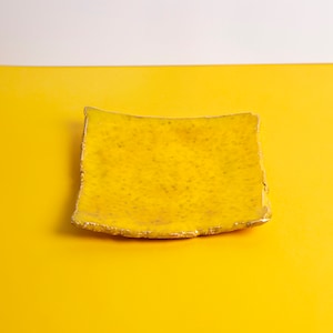 Puede incluir: Un plato de cer&aacute;mica amarillo con una forma ligeramente irregular y un borde dorado. El plato est&aacute; sobre una superficie amarilla.