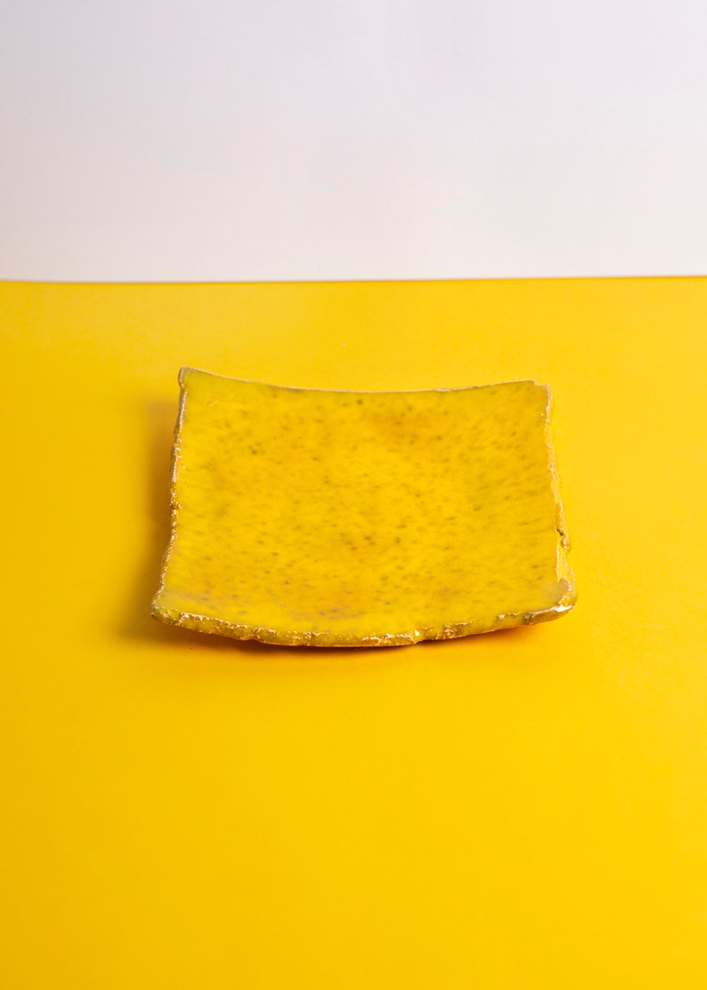 Puede incluir: Un plato de cer&aacute;mica amarillo con una forma ligeramente irregular y un borde dorado. El plato est&aacute; sobre una superficie amarilla.