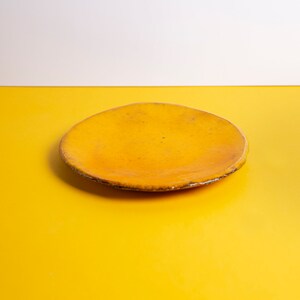 Puede incluir: Un plato de cer&aacute;mica amarillo con un borde ligeramente irregular. El plato est&aacute; sobre una superficie amarilla.