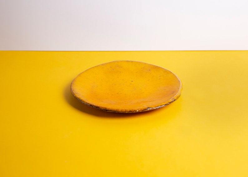 Puede incluir: Un plato de cer&aacute;mica amarillo con un borde ligeramente irregular. El plato est&aacute; sobre una superficie amarilla.