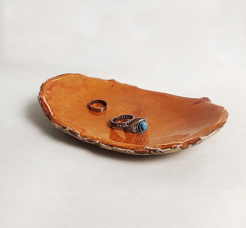 Puede incluir: Un peque&ntilde;o plato de cer&aacute;mica de forma ovalada con un esmalte naranja r&uacute;stico. Dos anillos descansan sobre el plato, uno con una piedra turquesa.
