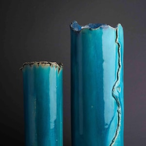 May include: Two teal blue ceramic vases with an uneven, textured rim. The taller vase has a crack running down the side.