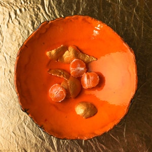 May include: Orange ceramic bowl with a glossy orange glaze. The bowl contains orange segments and peels.