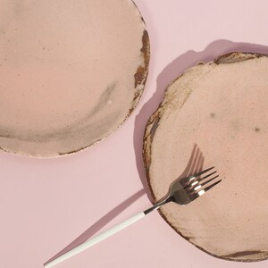 Puede incluir: Dos platos de cer&aacute;mica rosa con una superficie rugosa y texturizada y un tenedor plateado con mango blanco sobre un fondo rosa.