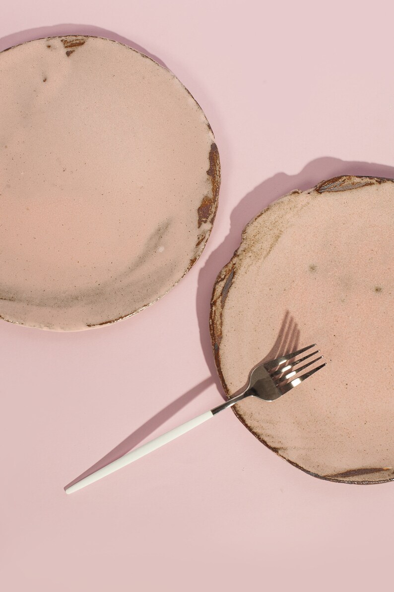 Puede incluir: Dos platos de cer&aacute;mica rosa con una superficie rugosa y texturizada y un tenedor plateado con mango blanco sobre un fondo rosa.