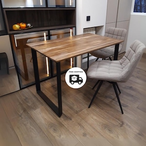 May include: A wooden dining table with a black metal frame and two gray upholstered chairs. The table has a natural wood grain finish and the chairs have a tufted design.