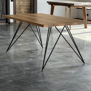Op de afbeelding: Een houten eettafel met een natuurlijke afwerking en zwarte metalen poten. De tafel heeft een rechthoekig blad en een eenvoudig, modern ontwerp.