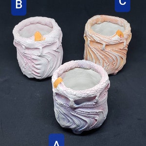 May include: Three small, decorative, ceramic pots with a textured, swirled design. The pots are in shades of pink, white, and orange.