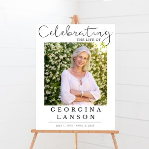 May include: A white memorial sign with black text that reads "Celebrating the Life of Georgina Lanson July 1, 1970 - April 3, 2035". A photo of a woman with light hair is in the centre of the sign.