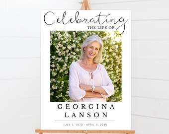 Könnte beinhalten: Ein weißes Gedenkschild mit schwarzem Text, der "Celebrating the Life of Georgina Lanson July 1, 1970 - April 3, 2035" lautet. Ein Foto einer Frau mit hellem Haar befindet sich in der Mitte des Schildes.