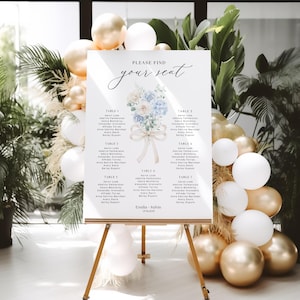 May include: A wedding seating chart on a wooden easel. The sign reads "Please find your seat" with a floral illustration. The background features gold and white balloons and lush greenery, creating an elegant and celebratory atmosphere.