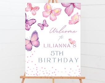 May include: Welcome to Lilianna's 5th Birthday sign with a white background and pink and purple butterflies. The sign has pink and gold confetti.