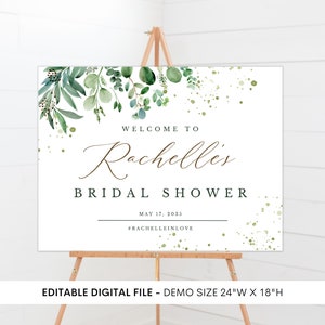 May include: A white welcome sign with green watercolor foliage and gold glitter accents. The text reads "Welcome to Rachelles Bridal Shower May 17, 2035 #Rachelleinlove". The sign is 24 inches wide by 18 inches high.