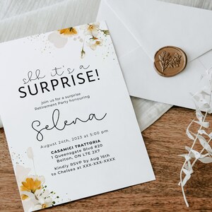 May include: A white invitation card with a floral design and gold accents. The text on the card reads "Shh it's a SURPRISE!" and includes details for a retirement party honoring Selena. The card is on a wooden surface with a white envelope and a gold wax seal.