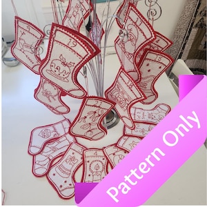 May include: A set of 24 red and white felt Christmas stocking ornaments with embroidered designs. The ornaments are hanging on a metal stand. The ornaments are numbered 1 through 24. The text "Pattern Only" is written on a pink banner.