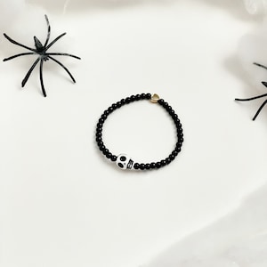 May include: A black beaded bracelet with a white skull charm and a gold heart charm.