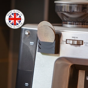 May include: A close-up of a silver coffee grinder with a black bean hopper and a silver grind size adjustment knob. The grinder has a label that says "Made in the UK" and a sticker that says "8000 Max".