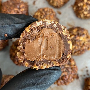 May include: A close-up of a chocolate truffle with a hazelnut and chocolate coating. The truffle is cut in half, revealing a smooth, creamy chocolate filling.