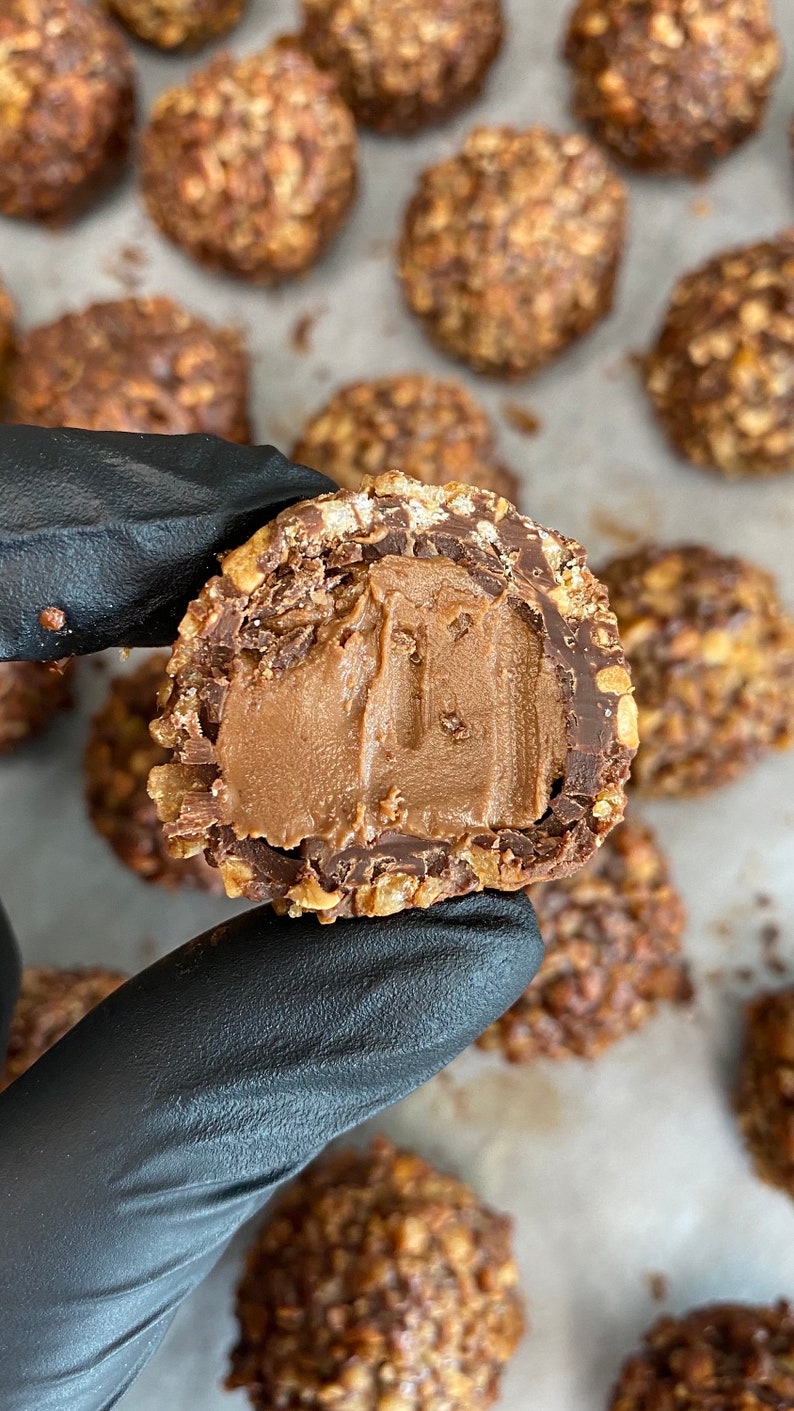 May include: A close-up of a chocolate truffle with a hazelnut and chocolate coating. The truffle is cut in half, revealing a smooth, creamy chocolate filling.