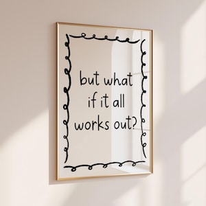 May include: A framed print with the words "but what if it all works out?" in black script. The text is centered on a cream background, framed by a black, wavy border and a gold frame. The print is hanging on a white wall.