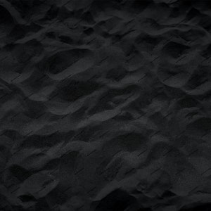 May include: A close-up of black sand with a textured surface. The sand is smooth and appears to be very fine.