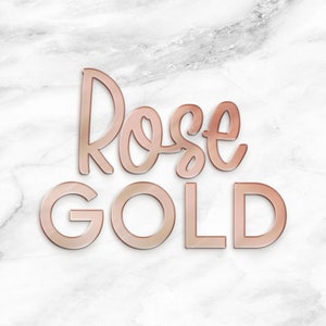 May include: Rose Gold text in a stylized font on a white marble background.