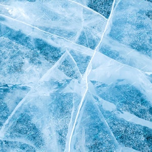 May include: Close-up of cracked ice with a blue hue. The ice is fractured with white lines creating geometric shapes. The texture of the ice is rough and uneven, with a slightly transparent quality. The overall effect is a cool, natural, and abstract pattern.