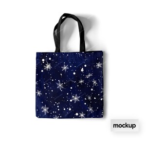 May include: A blue tote bag with a white snowflake pattern. The bag has black handles and the word "mockup" is printed in white on a white background below the bag.