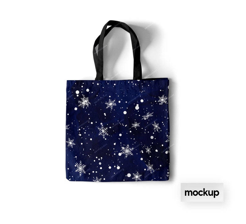 May include: A blue tote bag with a white snowflake pattern. The bag has black handles and the word "mockup" is printed in white on a white background below the bag.