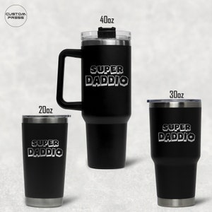 Może przedstawiać: Trzy czarne kubki ze stali nierdzewnej z srebrnym paskiem wokół dna. Kubki są oznaczone tekstem "SUPER DADDIO" w białym, blokowym kroju pisma. Kubki mają pojemność 20 uncji, 30 uncji i 40 uncji.
