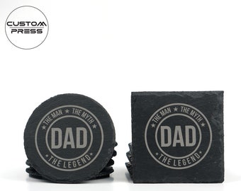 Puede incluir: Juego de seis posavasos de pizarra negra con un diseño grabado en gris. El diseño presenta un círculo con el texto "The Man The Myth Dad The Legend".