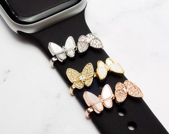 Pode incluir: Uma pulseira de relógio preta com quatro pingentes em forma de borboleta. Os pingentes são prateados, dourados, de ouro rosa e brancos. Os pingentes são adornados com strass.