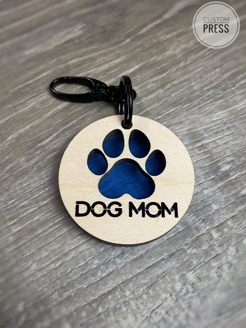 May include: A wooden keychain with a blue paw print cutout and the text "DOG MOM" engraved on it.