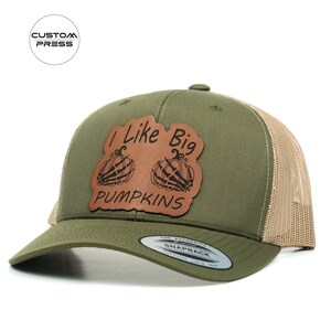 May include: Olive green and tan trucker hat with a leather patch. The patch features the text "I Like Big PUMPKINS" with two pumpkin illustrations. The hat has a curved brim and a snapback closure.