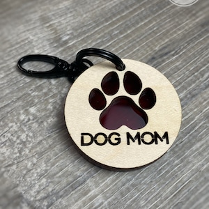 May include: A wooden keychain with a red paw print and the text "DOG MOM" engraved on it. The keychain has a black metal ring.