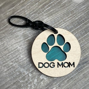 May include: A wooden keychain with a teal paw print and the text "DOG MOM" engraved on it. The keychain has a black metal ring.