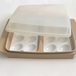 May include: A beige and white plastic egg container with a clear lid. The container has two sections, each with six egg-shaped indentations. The lid is slightly ajar, revealing the egg holders.