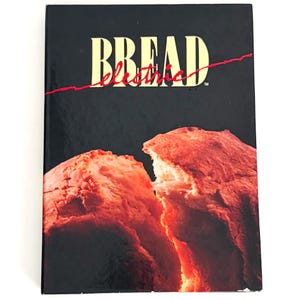 May include: A hardcover book with a black cover featuring the word BREAD in large yellow capital letters and the word electric in red cursive script. Below the text is a photograph of a loaf of bread broken in half with a glowing orange center.