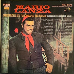 May include: A vintage vinyl record album cover featuring Mario Lanza. The album cover has a portrait of Lanza wearing a dark jacket and a red scarf. The album title is in large orange letters, with a list of songs on the right.
