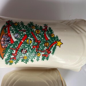 May include: Two white ceramic Christmas themed bowls with a gold trim. The larger bowl features a Christmas tree with red bows, candy canes, and ornaments. The smaller bowl is plain.