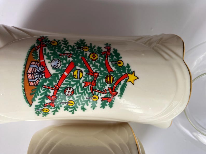 May include: Two white ceramic Christmas themed bowls with a gold trim. The larger bowl features a Christmas tree with red bows, candy canes, and ornaments. The smaller bowl is plain.