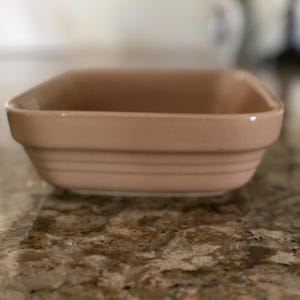 May include: A rectangular ceramic baking dish in a solid light tan color. The dish features a smooth, glossy finish with three horizontal embossed ridges running along the exterior sides, providing a simple and functional design for kitchen use.