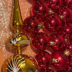 May include: A gold Christmas tree topper with white accents and a cluster of red ornaments. The topper has a long, pointed tip and a decorative globe shape. The red ornaments are round and shiny.